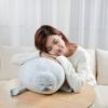 Une jeune femme souriante se blottit contre un coussin en forme de phoque gris.