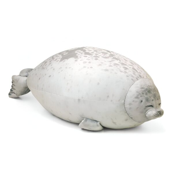 Un coussin en forme de phoque gris avec des taches blanches, allongé sur le ventre.