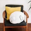 Un coussin en forme de phoque gris, endormi sur un fauteuil avec un coussin jaune.