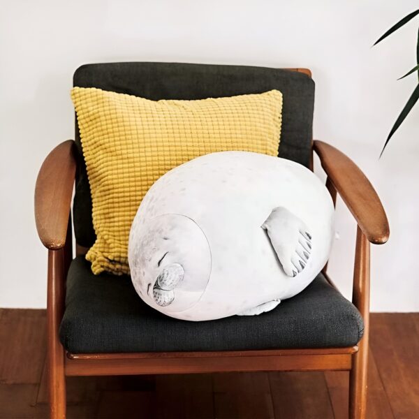 Un coussin en forme de phoque gris, endormi sur un fauteuil avec un coussin jaune.