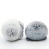Deux phoques en peluche, l'un blanc et l'autre gris, sont couchés sur un fond blanc. Le phoque blanc est allongé sur le dos, les yeux fermés. Le phoque gris est assis sur ses pattes, les yeux ouverts.