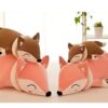 Trois adorables peluches renards, deux roses et une marron, s'amusent à dormir en s'entassant l'une sur l'autre.