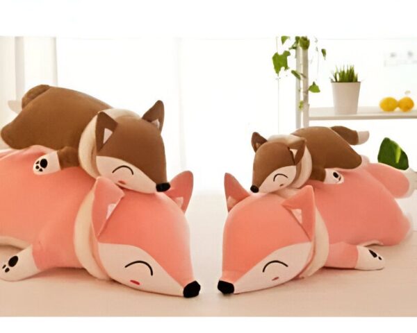 Trois adorables peluches renards, deux roses et une marron, s'amusent à dormir en s'entassant l'une sur l'autre.