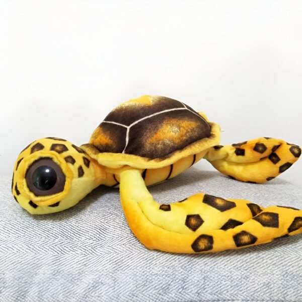Une tortue en peluche jaune et brune avec de grands yeux noirs.
