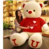 Une femme souriante enlaçant un grand ours en peluche blanc portant un pull rouge avec le mot "Love" écrit dessus. L'ours a des "I" et "U" sur ses pieds.