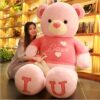 Une jeune femme assise avec un grand ours en peluche rose portant un t-shirt "Love" et les mots "I U" écrits sur ses pieds.