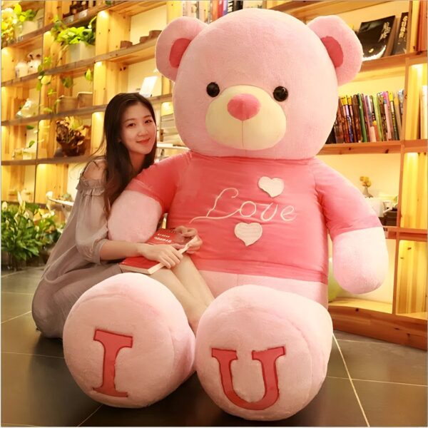 Une jeune femme assise avec un grand ours en peluche rose portant un t-shirt "Love" et les mots "I U" écrits sur ses pieds.