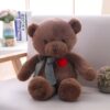 Un gros ours en peluche marron assis sur un canapé blanc avec un nœud vert et blanc autour du cou et un cœur rouge sur la poitrine.