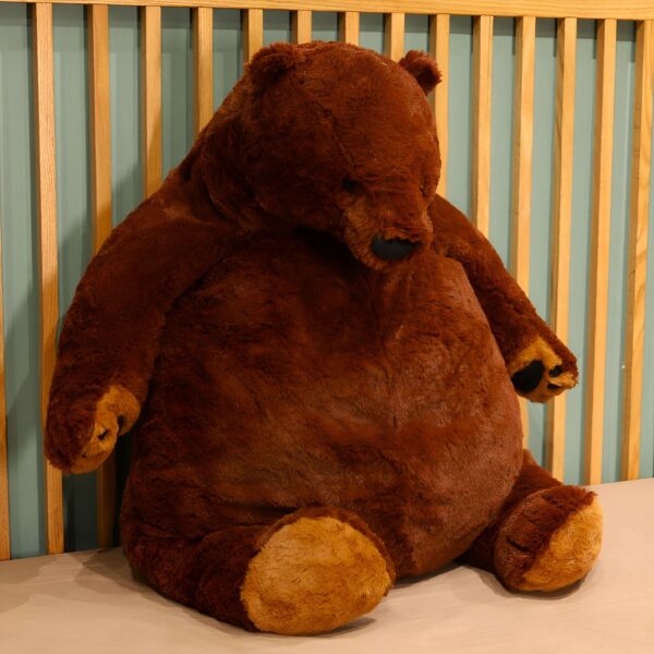 Un gros ours en peluche brun assis sur un canapé en bois.