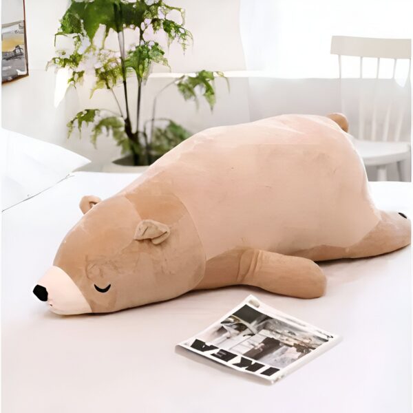 peluche-ours-marron-qui-dort-2a Un grand ours en peluche brun allongé sur un lit blanc.