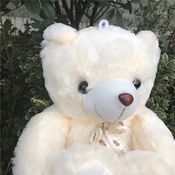 Un gros ours en peluche blanc avec un noeud autour du cou, assis dans l'herbe.