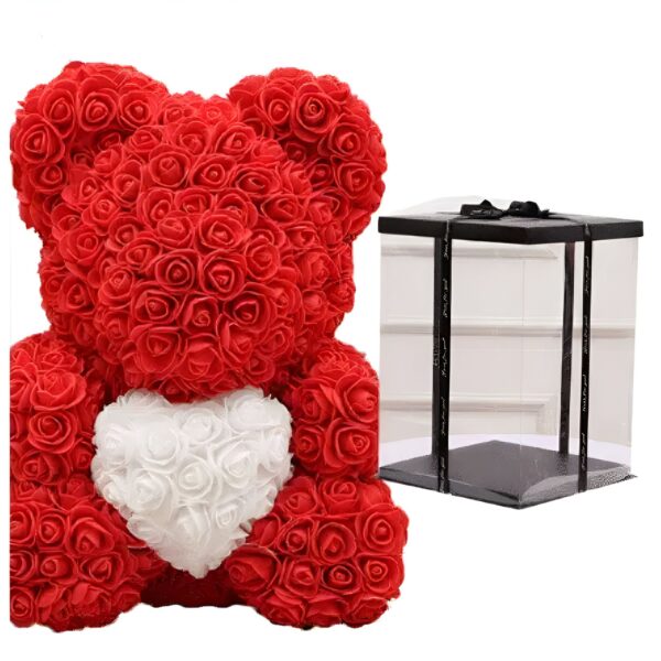Un ours en peluche rouge fait de roses artificielles tenant un cœur blanc en roses. L'ours est livré dans une boîte transparente avec un ruban noir.