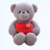 Un ours en peluche gris assis tenant un cœur rouge avec le mot "LOVE" écrit dessus.