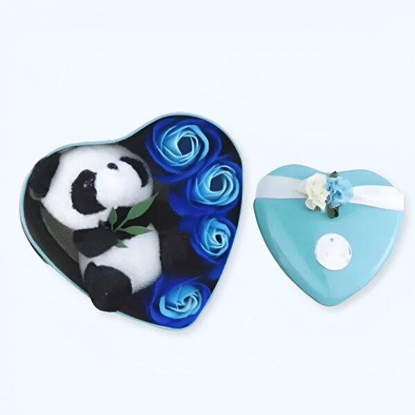 Un ourson panda en peluche assis dans un coffret en forme de cœur bleu entouré de roses bleues. Le coffret est ouvert et l'ourson est visible. Il y a un autre coffret en forme de cœur bleu fermé à côté.