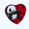 Un ours en peluche panda noir et blanc dans une boîte en forme de cœur rouge avec des roses rouges.