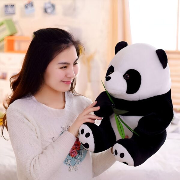Une jeune femme souriante tenant une peluche de panda noire et blanche qui tient une branche de bambou verte dans sa patte.