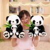 Une jeune femme tient deux peluches pandas noirs et blancs avec des bébés pandas dans leurs bras. Les pandas tiennent des feuilles de bambou vertes.