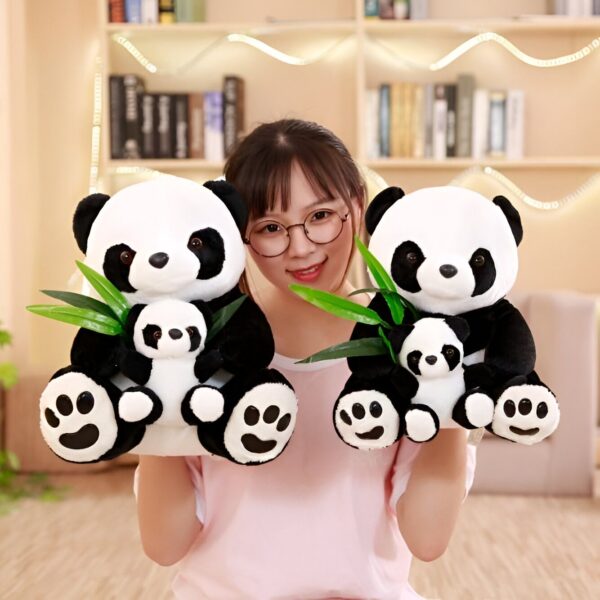 Une jeune femme tient deux peluches pandas noirs et blancs avec des bébés pandas dans leurs bras. Les pandas tiennent des feuilles de bambou vertes.