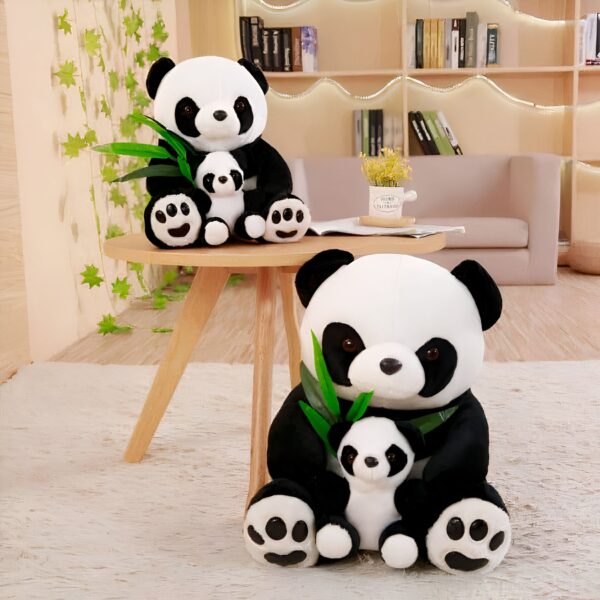 Deux ours en peluche panda, un grand et un petit, assis sur une table en bois avec des feuilles de bambou. Le plus grand porte le plus petit. Ils sont tous les deux noirs et blancs.