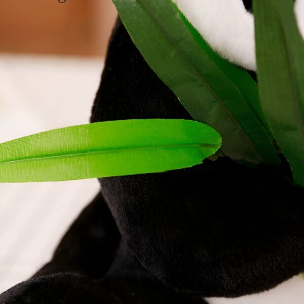 Une feuille de bambou verte se trouve sur le dos d'un panda en peluche noir et blanc.