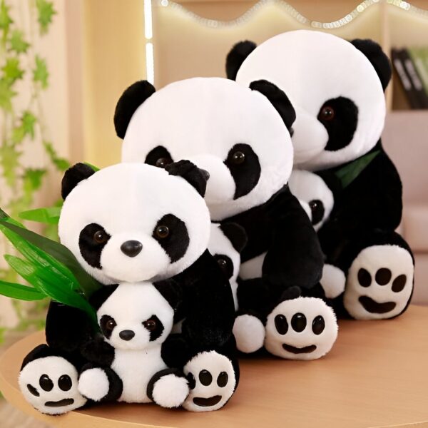 Une collection de quatre peluches pandas de différentes tailles, assis sur une table. Les pandas sont tous noirs et blancs avec de gros yeux noirs. Le plus grand panda porte un bébé panda dans ses bras.