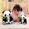 Une jeune femme regarde deux peluches de pandas. La plus grande peluche est une mère panda tenant son petit. La plus petite peluche est un autre panda tenant son petit.