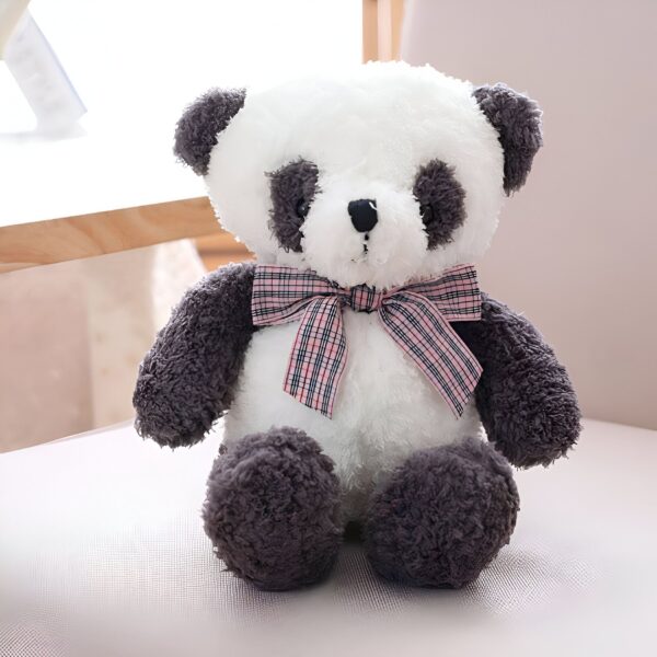 Une peluche de panda avec un noeud rose et blanc assis sur un fauteuil.