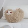 Un coussin en forme de paresseux en peluche beige avec un visage souriant.