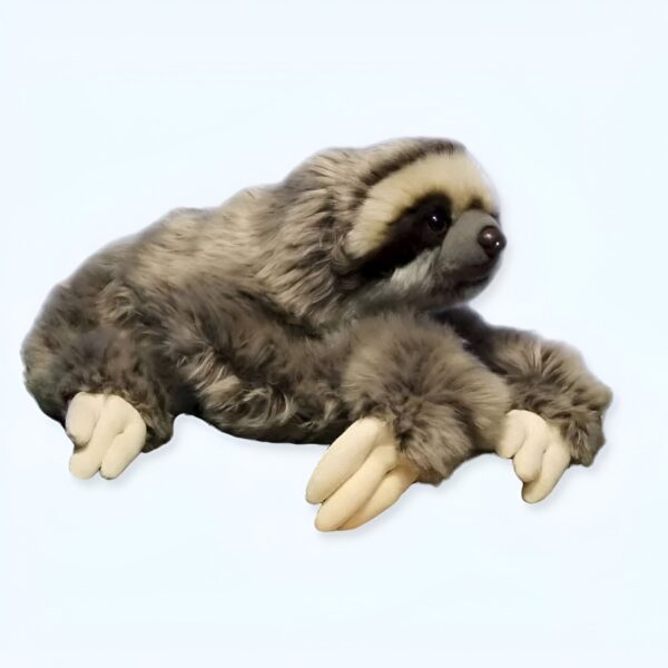 Une peluche de paresseux en position couchée, regardant vers la droite. Il est en fourrure grise et beige avec des pattes légèrement beige.