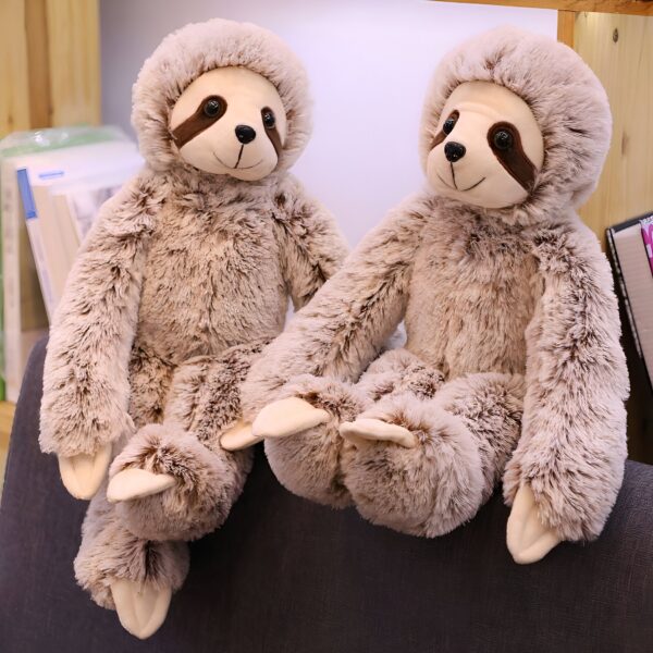 Deux adorables peluches paresseux en fourrure brune assis côte à côte sur un canapé.