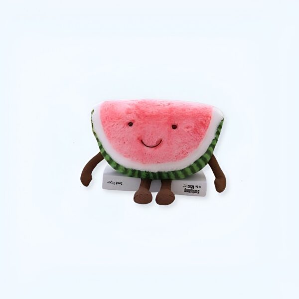 peluche-pasteque-fruit-jouet-enfant-doux-et-confortable-1a-1 Peluche pastèque souriante avec des bras et des jambes, assise sur un livre.
