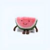 peluche-pasteque-fruit-jouet-enfant-doux-et-confortable-1a-4 Peluche pastèque souriante avec des bras et des jambes, assise sur un livre.