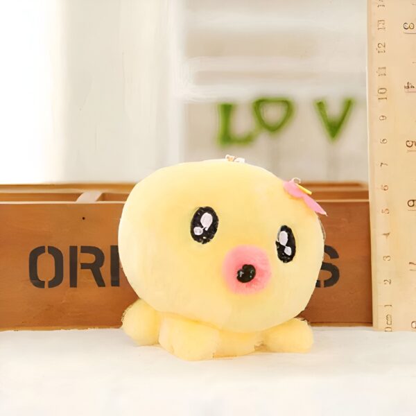 Une peluche jaune en forme de poulpe avec des yeux noirs et une bouche rose, devant une boîte en bois et un mur avec le mot "LOVE" écrit en vert.
