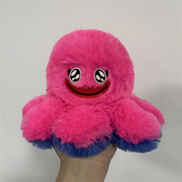 Une peluche rose en forme de pieuvre avec un grand sourire brodé. La pieuvre est douce et moelleuse et a des tentacules bleus.
