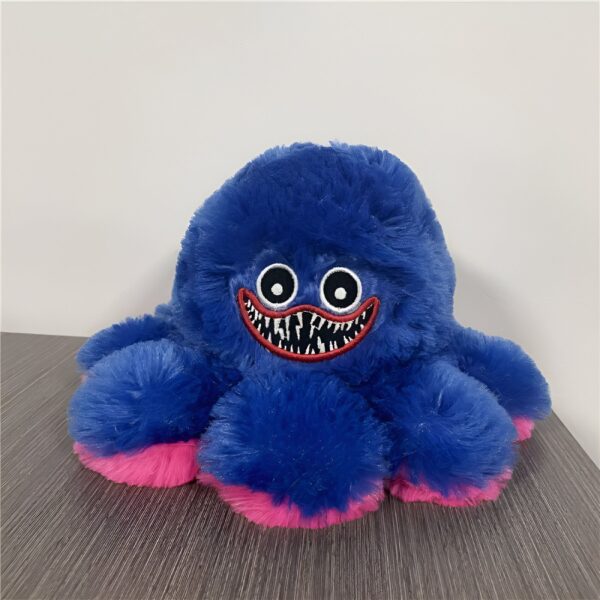 Peluche de pieuvre bleu foncé à fourrure avec des yeux noirs, une bouche rouge et des dents pointues blanches, avec une bordure rose sur ses bras.