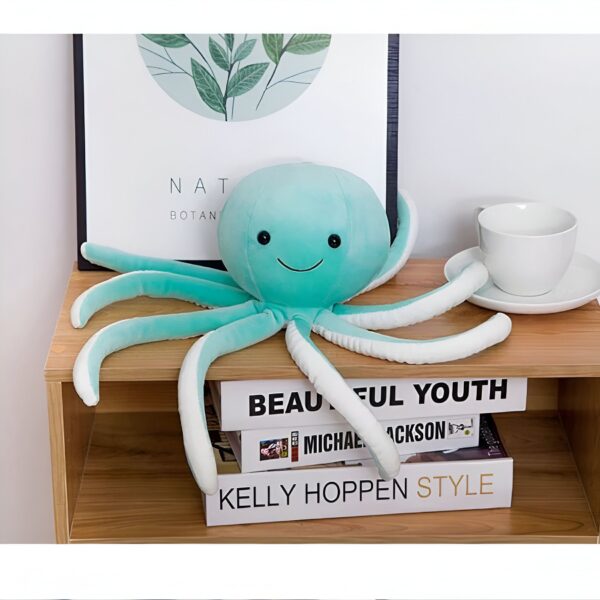 Une peluche de pieuvre verte souriante avec des tentacules blancs posée sur une étagère en bois.
