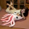 Une femme souriante est allongée sur un lit avec un grand calmar rose en peluche.