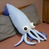Une peluche de calmar bleu avec de grands yeux noirs et des tentacules violets sur un lit.