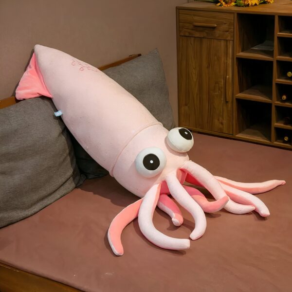 Un gros calamar rose en peluche avec de grands yeux noirs et des tentacules roses sur un lit.