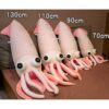 Une collection de peluches en forme de calmar de différentes tailles. Les peluches sont roses et ont des yeux noirs. Elles sont disposées sur un lit.