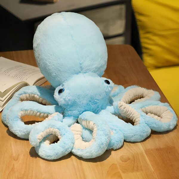 Une peluche de pieuvre bleue à poils doux avec des yeux noirs et blancs posée sur une table en bois.
