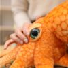Gros plan sur l'œil d'une peluche de pieuvre orange. L'œil est grand et vert avec des pupilles noires. La peluche est douce et moelleuse.
