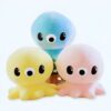 Trois adorables peluches poulpes dans des couleurs pastel : bleu, jaune et rose. Ils ont de grands yeux noirs et des sourires amicaux. Ces peluches sont parfaites pour les enfants de tous âges.