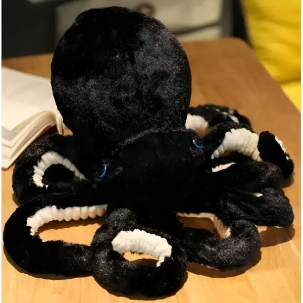 Une peluche de pieuvre noire avec des yeux bleus et des tentacules blancs.