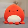 peluche-pieuvre-oreiller-doux-2a-5 Un adorable peluche rouge en forme de poulpe souriant sur un lit gris.