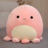 peluche-pieuvre-oreiller-doux-3a-6 Une peluche rose en forme de pieuvre souriante avec de grands yeux noirs.
