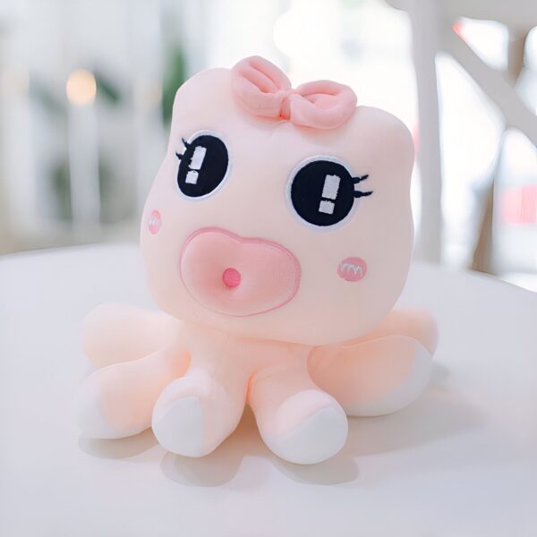 Une peluche rose en forme de poulpe avec un nœud rose sur la tête, de grands yeux noirs et un sourire.