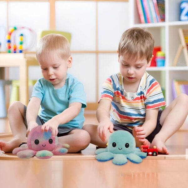 peluche-pieuvre-reversible-emoji-heureux-en-colere-cadeau-enfant-10a Deux jeunes garçons jouent avec des peluches pieuvres colorées sur le sol. L'un a une pieuvre arc-en-ciel et l'autre a une pieuvre bleu clair.