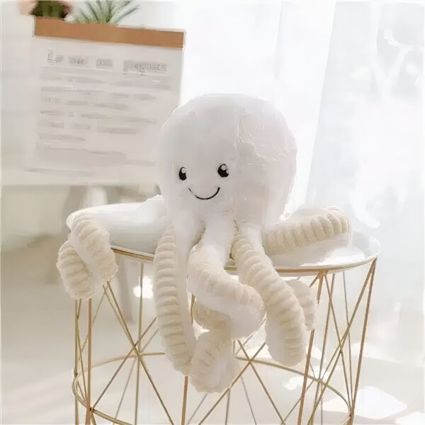 Une peluche de pieuvre blanche avec un sourire souriant assis sur un tabouret en métal doré.