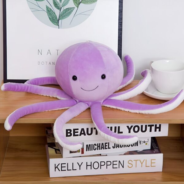 Une peluche de poulpe violette avec un sourire sur un étagère en bois avec des livres.